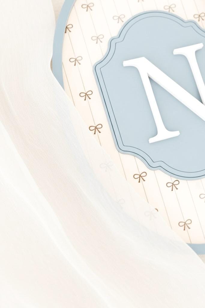 Letter 'N' in a decorative frame with a light blue background and gold ribbons.