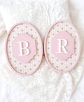 Two pink decorative plates with letters 'B' and 'R' on a textured white background