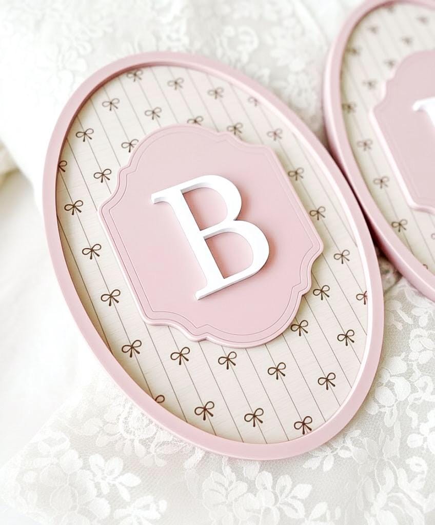 Decorative pink acrylic sign with a white letter 'B' on a white lace background