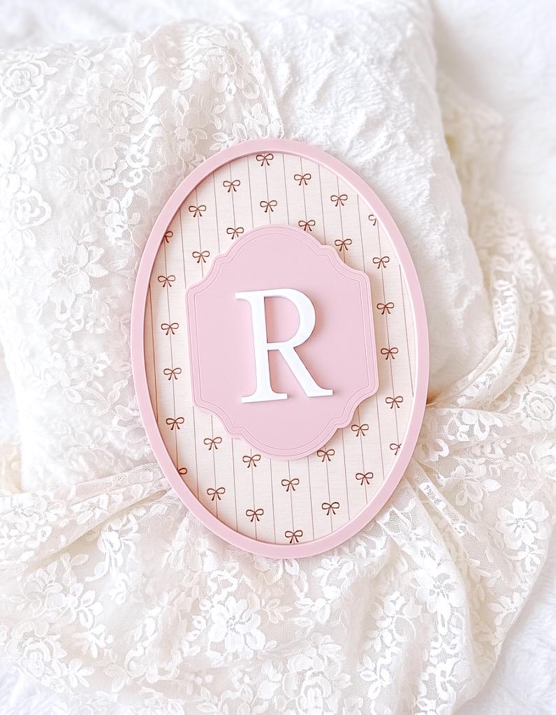 pink acrylic frame with a white letter 'R' on a lace background